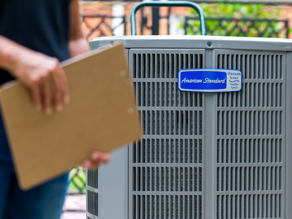Person holding clipboard standing next to an air conditioning unit.